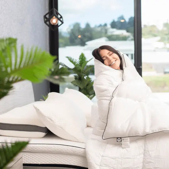 Mujer sonriendo envuelta en una cómoda colcha de productos de bambú en una habitación bien iluminada, mostrando los beneficios de dormir con productos de bambú.