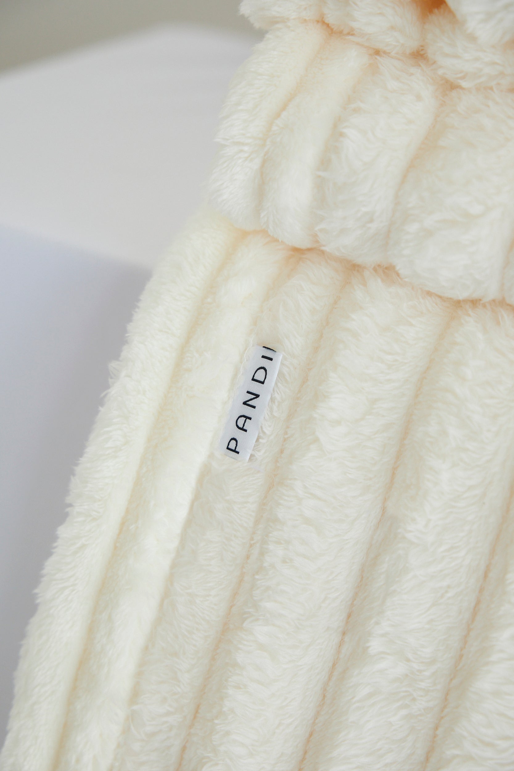 Manta Cuzy - Crema, perfecta para abrigarte con su manta de franela suave, ofreciendo comodidad y estilo en tu hogar.