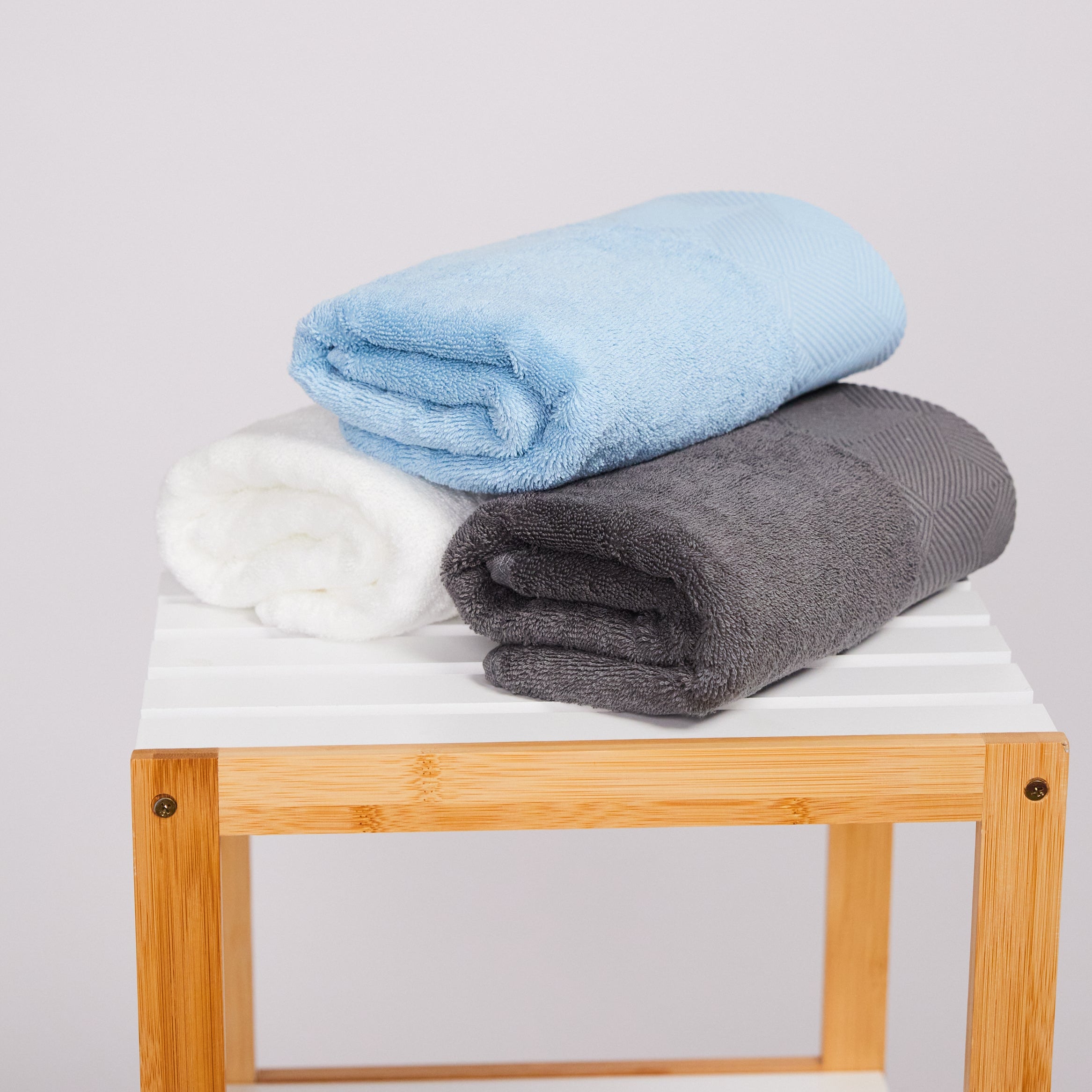 Variedad de toallas de mano PANDI en colores adicionales, apiladas en una estantería de bambú, ideal para un baño moderno.