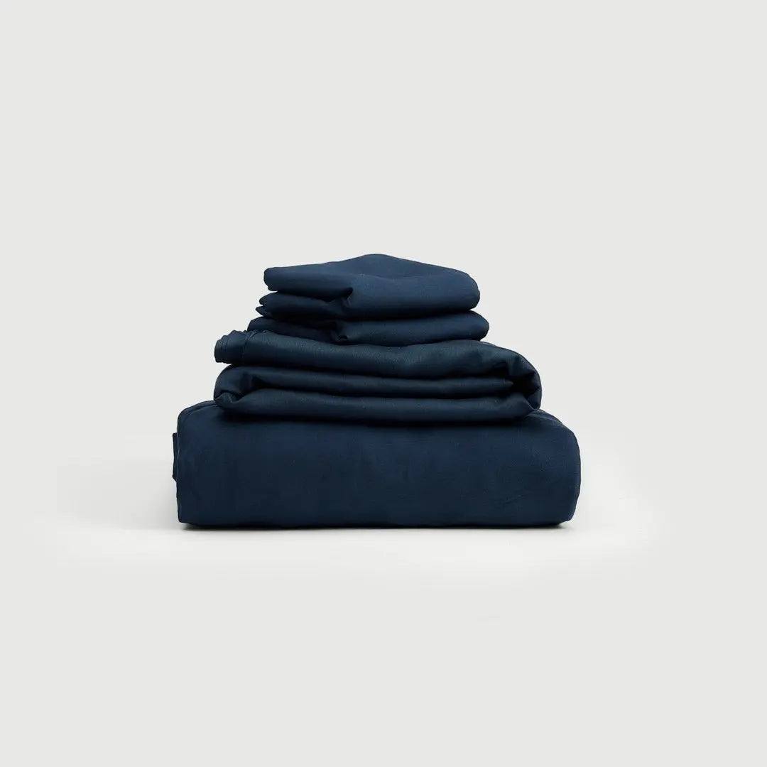 Set de Sábanas 100% Bambú en elegante azul marino, apiladas de manera organizada, mostrando la suavidad y frescura natural del material.