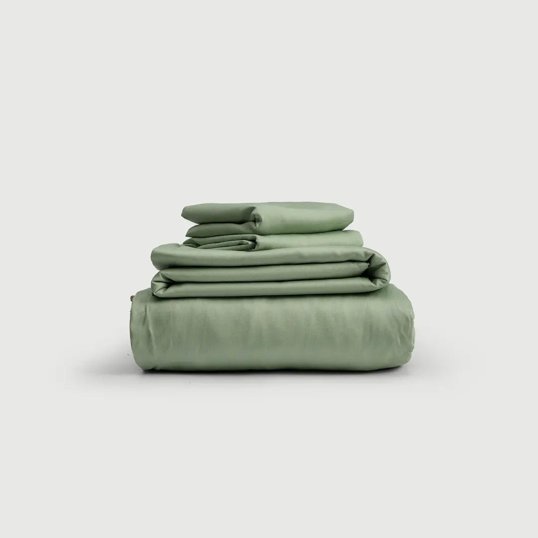 Set de sábanas 100% bambú en vibrante color verde, apiladas de manera organizada, ideales para un descanso reparador.