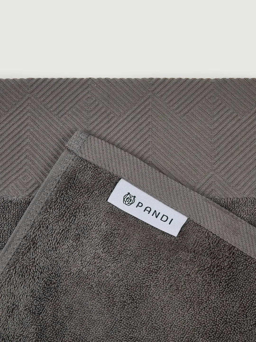 Detalles de la TOALLA DE MANO Gris Oscuro de PANDI, centrando en el logo y los ribetes, perfecta para añadir un toque de lujo a tu hogar.