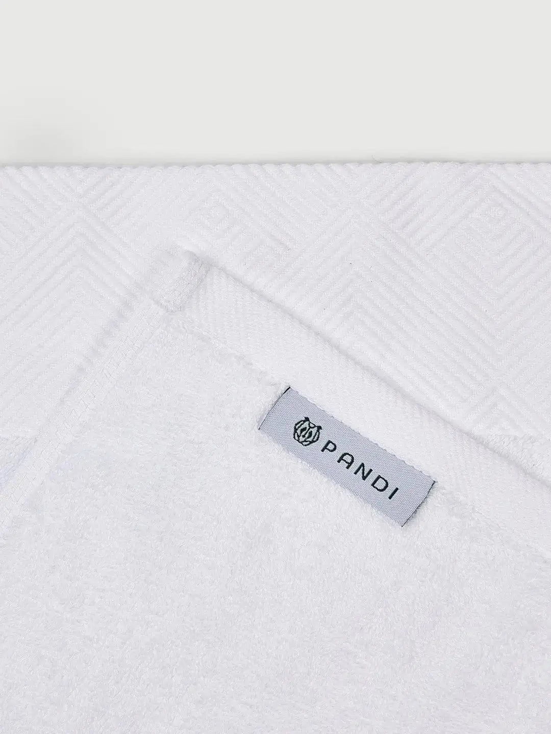 Detalle de las toallas de mano PANDI en blanco, resaltando la etiqueta de la marca y el diseño texturizado para un toque de lujo.
