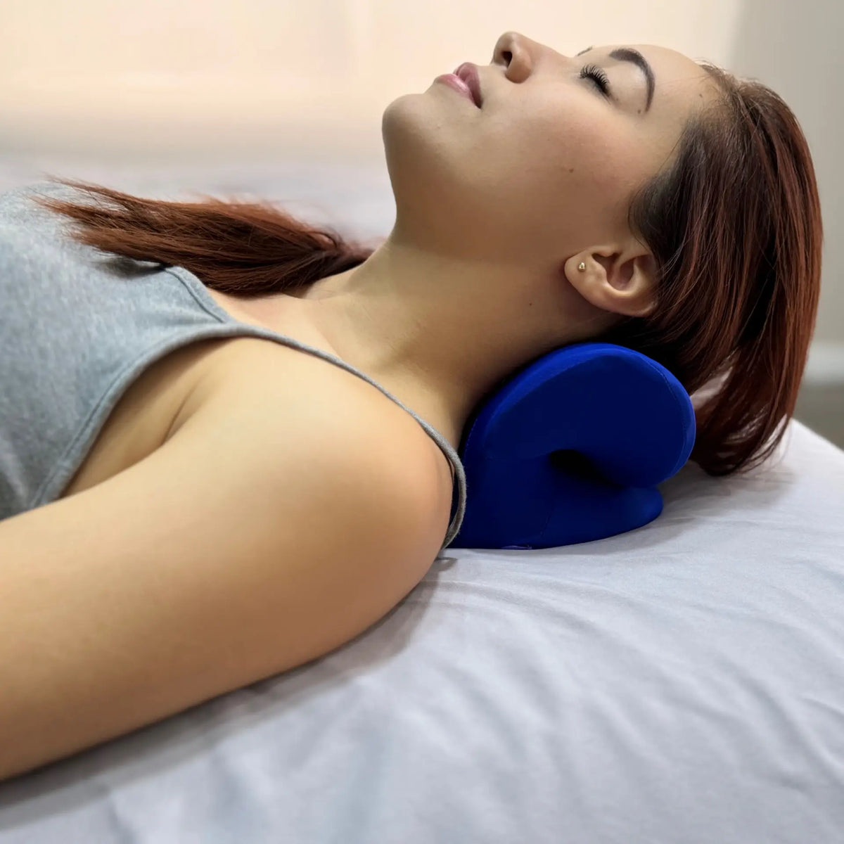 Mujer usando el Dispositivo de Tracción Cervical PANDI, apoyando su cuello con el dispositivo azul durante una sesión de relajación en una superficie suave.